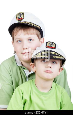 Zwei Jungs in grünen T-Shirts und weißen Meeresspiegelkappen mit Augen, die irgendwo nach oben schauen, konzentrieren Sie sich auf den kleinen Jungen Stockfoto