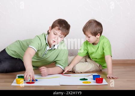 Zwei Jungs in den grünen T-Shirts zeichnen mit ihren Fingern Farbfarben auf die Papierbögen Stockfoto