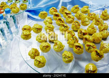 Profiterolen gefüllt mit Salaten und Flaschen mit Wasser auf einem Sammelbecken. Stockfoto