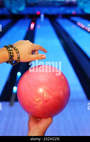 Hände des Mannes, der roten Ball hält und sich darauf vorbereitet, in den Bowlingclub zu werfen Stockfoto