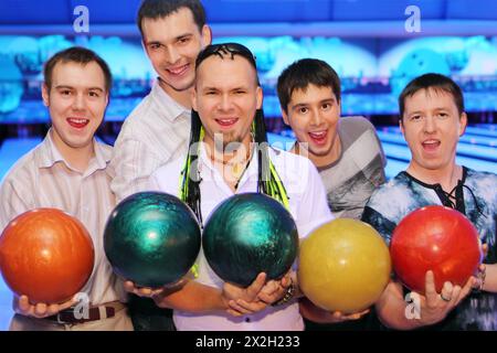 Fünf glückliche Männer halten im Bowlingclub Bälle, Freunde entspannen sich zusammen Stockfoto