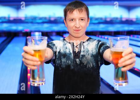 Ein glücklicher junger Mann hält zwei große Gläser Bier im Bowlingclub Stockfoto