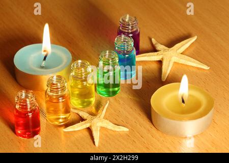 Reihe von sechs Flaschen mit farbigen Aromaölen, Kerzen und Sternenfischen auf dem Tisch Stockfoto