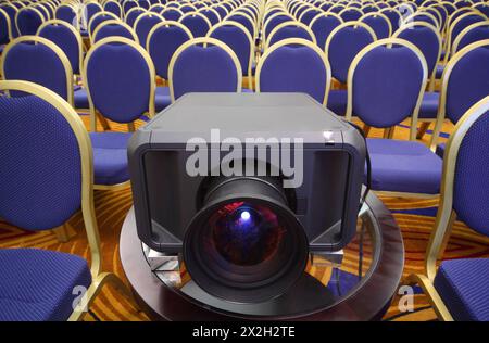 Schwarzer Projektor in der Mitte der Reihen gelb-blauer Stühle im hellen Konferenzsaal Stockfoto