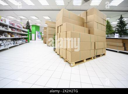 Regale mit verschiedenen künstlichen Weihnachtsbäumen und Souvenirs im großen Supermarkt mit Kisten in der Mitte Stockfoto