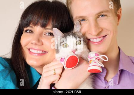 Ein lächelnder junger Ehemann und eine Frau halten die Katze in roten Stiefeln; konzentrieren Sie sich auf die Katze Stockfoto