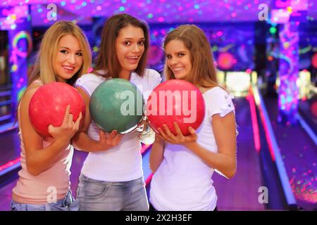 Drei lächelnde Mädchen mit Bällen stehen im Bowlingclub und bereiten sich auf das Spiel vor Stockfoto