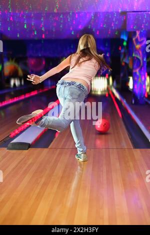 Der Rücken des Mädchens trägt Jeans und weißes T-Shirt und macht Ballwurf im Bowlingclub Stockfoto