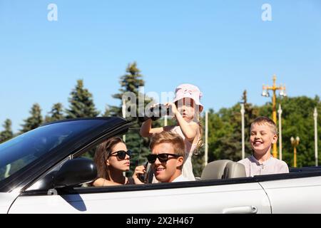 Wunderschöner Vater, Mutter und zwei Kinder fahren in einem Cabrio und spielen Spione Stockfoto