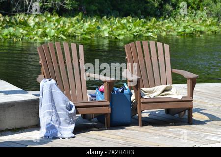 Zwei Adirondack-Stühle, ein Handtuch und eine Tragetasche, sitzen auf der Promenade neben dem Wekiva River in Longwood, Florida. Stockfoto