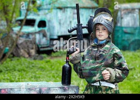 der-junge-in-der-tarnung-h-lt-ein-paintball-gewehrlauf-hoch-und-sagt