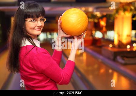 Glückliches Mädchen mit gelben Ballständern im Bowlingclub und bereit zum Werfen Stockfoto