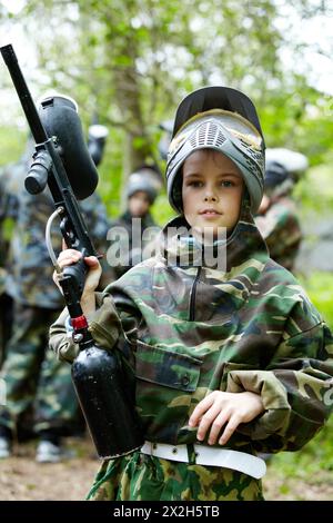 der-junge-in-der-tarnung-h-lt-ein-paintball-gewehrlauf-hoch-und-sagt