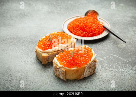 Kleine Metallplatte mit rotem Lachskaviar und zwei Kaviar-Toasts Canape auf grauem Betonhintergrund, festliche Luxus-Delikatesse und Vorspeise Stockfoto