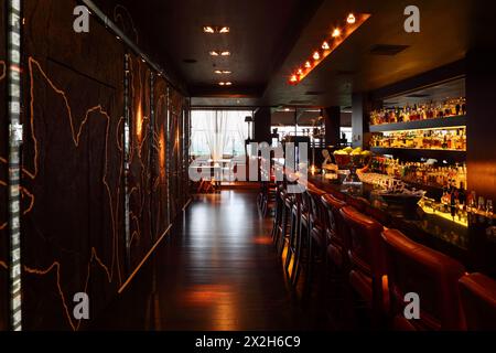 Bartheke mit roten Stühlen in einem leeren, komfortablen Restaurant; viele Getränke in den Regalen Stockfoto