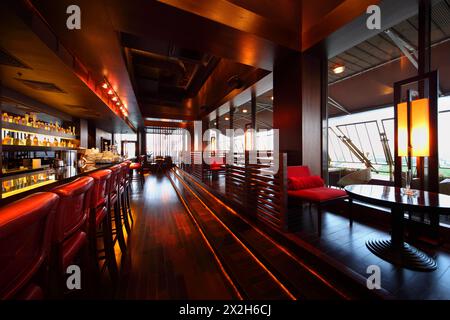 Reihe von Tischen, roten Stühlen und Bartheke mit roten hohen Stühlen in leerem, gemütlichem Restaurant Stockfoto