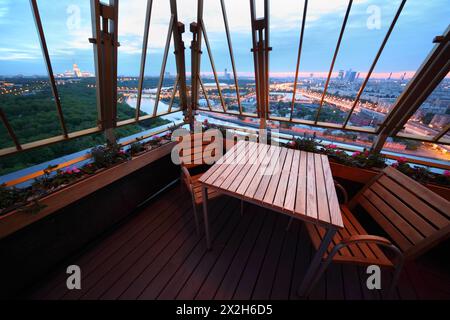 Holzstühle und Tisch auf der Terrasse im Restaurant; Panoramablick auf Moskau am Abend Stockfoto