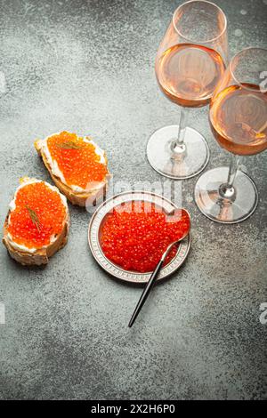 Kleine Metallplatte mit rotem Lachskaviar, zwei Kaviar Toast Canape, zwei Gläser Champagner von oben auf grauem Betonhintergrund, festlicher Luxus Stockfoto