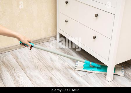 Die Hausfrau wischt den Boden unter dem Schrank. Nassreinigung des Fußbodens im Zimmer. Reinigung von Staub unter Schränken. Hochwertige Fotos Stockfoto