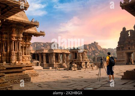 Ein männlicher Touristenfotograf an den antiken Ruinen der Steinarchitektur des Vijaya Vittala Tempels in Hampi, Karnataka, Indien mit stimmungsvollem Sonnenuntergang. Stockfoto