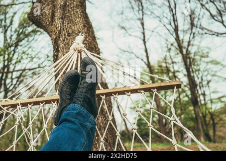 Mann, der sich in einer Hängematte am Baum liegend und entspannt, Jeans und schmutzige schwarze Sneakers trägt, selektiver Fokus Stockfoto