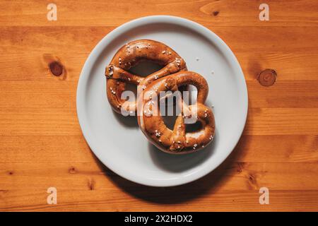 Blick von oben auf zwei frisch gebackene Brezeln auf einem Teller auf einem Holztisch Stockfoto