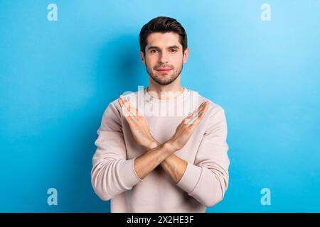 Porträt des ernsthaften protestierenden Mannes mit stilvoller Friseurkleidung beige Sweatshirt halten Hände gekreuzt isoliert auf blauem Hintergrund Stockfoto