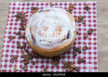 Zimtbrötchen mit Zuckerguss auf der Oberseite, serviert auf rot-weißer Serviette mit verstreuten Zimtstücken Stockfoto