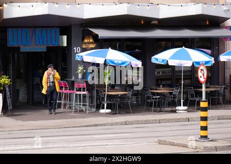 Basel, Schweiz - 18. April 2024: Ein Mann steht auf dem Bürgersteig vor dem Restaurant mit Außensitzen und Sonnenschirmen Stockfoto