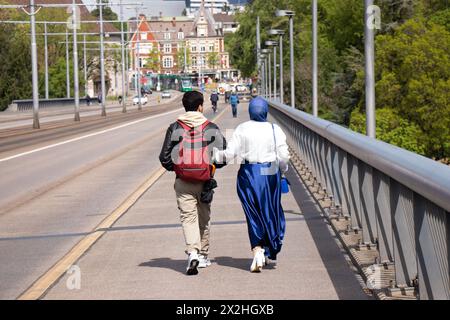 Basel, Schweiz - 18. April 2024: Junge muslimische Paare gehen Arm in Arm auf der Wettsteinbrücke, Rückansicht Stockfoto