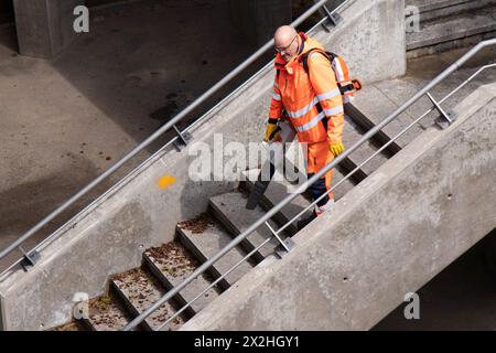 Basel, Schweiz - 18. April 2024: Ein Arbeiter in orangefarbener Uniform, der die Stadtbrückentreppe mit Laubbläser reinigt Stockfoto