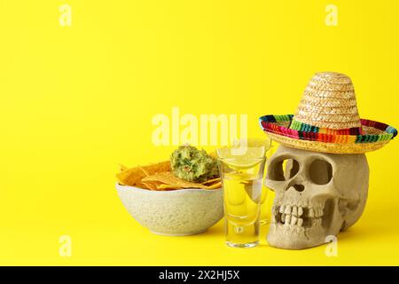 Mexikanischer Sombrero-Hut, menschlicher Schädel, Tequila, Nachos-Chips und Guacamole in Schüssel auf gelbem Hintergrund, Platz für Text Stockfoto