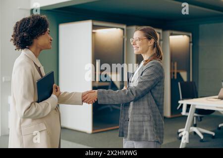 Stilvolle junge Geschäftsmanagerin mit Handschütteln begrüßt die Kundin im Büro Stockfoto