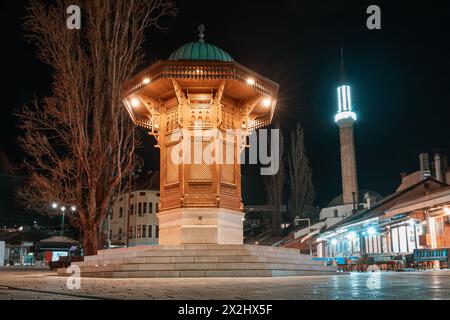 Historische Straßen von Sarajevos Bascarsija-Viertel bei Nacht, wo der beleuchtete Sebilj-Brunnen als zeitloses Wahrzeichen islamischer Architektur steht Stockfoto