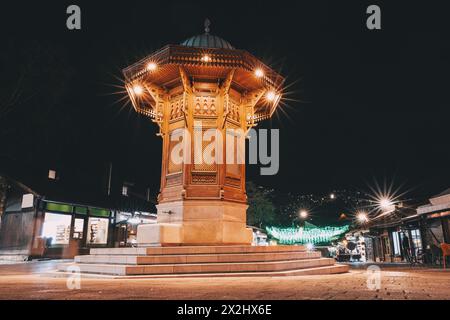 Historische Straßen von Sarajevos Bascarsija-Viertel bei Nacht, wo der beleuchtete Sebilj-Brunnen als zeitloses Wahrzeichen islamischer Architektur steht Stockfoto