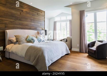 King size Bett mit grauem Leinentuch Kopfteil, Holzkohle Velours Sessel im Schlafzimmer mit Hickory Holz Dielen in einem luxuriösen Stockfoto