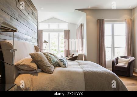 King size Bett mit grauem Leinentuch Kopfteil, Holzkohle Velours Sessel im Schlafzimmer mit Hickory Holz Dielen in einem luxuriösen Stockfoto