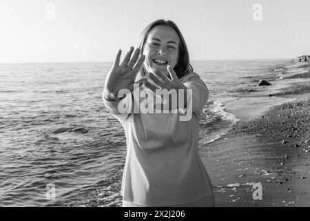 Eine Frau, die allein an einem Sandstrand an den Meereswellen steht, auf den Horizont blickt und die Meeresbrise an einem sonnigen Tag spürt. Schwarz-weiß Stockfoto