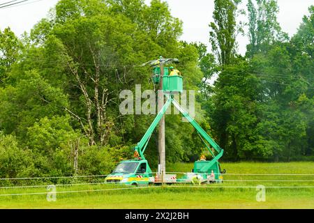 Bergerac, Frankreich - 27. April 2023: Zwei Energieversorger warten Freileitungen vor einem Hintergrund üppiger Grünflächen. Stockfoto