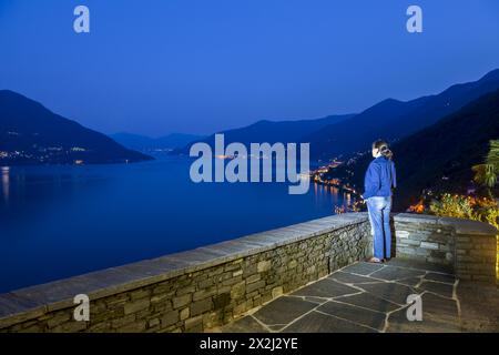 Frau Genießen Sie einen Panoramablick über den Alpensee Maggiore mit Berg in der Blauen Stunde in Ronco Sopra Ascona, Tessin, Schweiz Stockfoto
