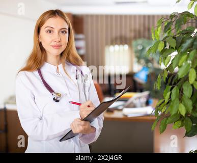 Die junge Therapeutin schreibt Notizen auf eine Tablette und steht in einem Büro Stockfoto