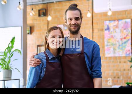 Ein paar Kollegen zu umarmen, Partner junger Mann und Frau in Schürzen am Arbeitsplatz Stockfoto