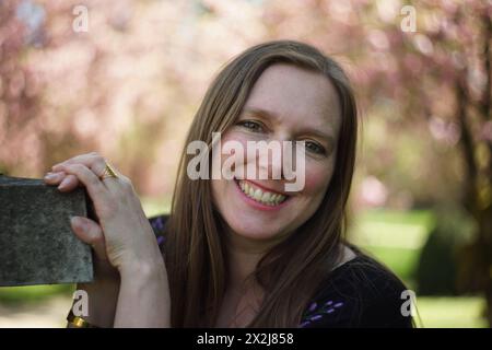 Porträt einer Frau, umgeben von den Zweigen eines dekorativen Kirschbaums, geschmückt mit zarten rosa Kirschblüten und üppig grün-gelben Blättern. S Stockfoto