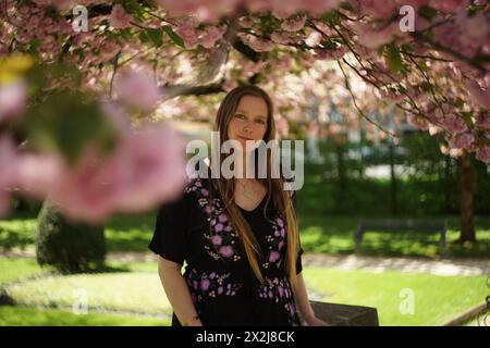 Porträt einer Frau, umgeben von den Zweigen eines dekorativen Kirschbaums, geschmückt mit zarten rosa Kirschblüten und üppig grün-gelben Blättern. S Stockfoto