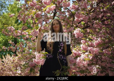 Porträt einer Frau, umgeben von den Zweigen eines dekorativen Kirschbaums, geschmückt mit zarten rosa Kirschblüten und üppig grün-gelben Blättern. S Stockfoto