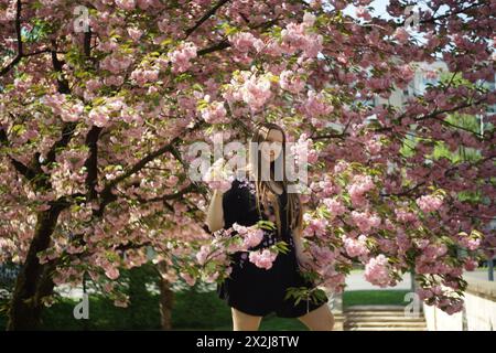 Porträt einer Frau, umgeben von den Zweigen eines dekorativen Kirschbaums, geschmückt mit zarten rosa Kirschblüten und üppig grün-gelben Blättern. S Stockfoto