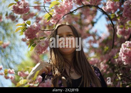 Porträt einer Frau, umgeben von den Zweigen eines dekorativen Kirschbaums, geschmückt mit zarten rosa Kirschblüten und üppig grün-gelben Blättern. S Stockfoto