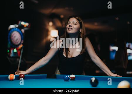 Junge Frau, die in einer schwach beleuchteten Bar mit farbenfroher Beleuchtung Pool spielt Stockfoto
