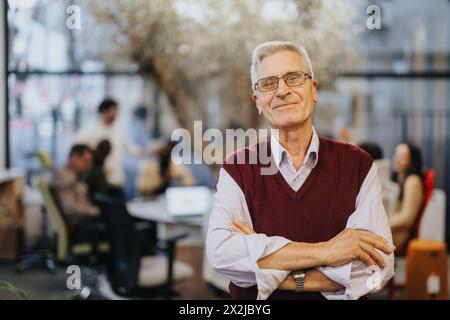 Ein selbstbewusster Geschäftsmann, der in einem modernen Büro steht. Er ist stolzer und positiver Leiter eines Unternehmens und zeigt Erfolg und Zufriedenheit mit seiner Arbeit. Stockfoto