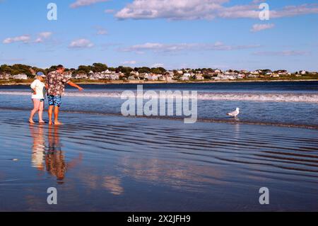 Ein älteres Paar spaziert am Strand und watscht an einem sonnigen Sommerurlaub im seichten Meereswasser an der Küste Stockfoto